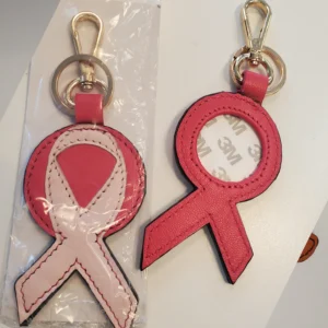 A pink ribbon keychain is shown in its packaging.
