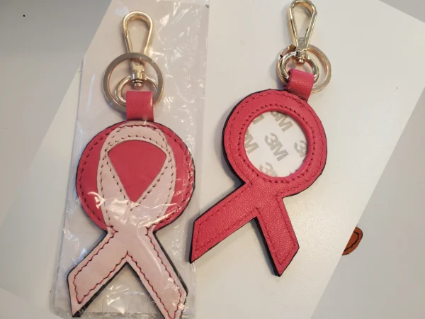 A pink ribbon keychain is shown in its packaging.