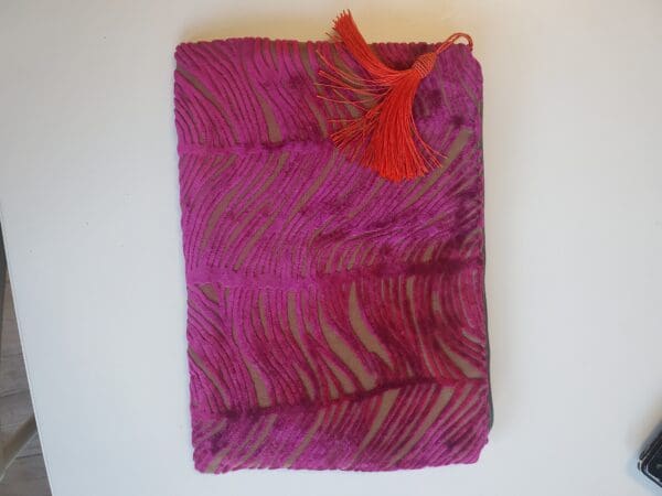 A purple bag with red tassels on top of it.