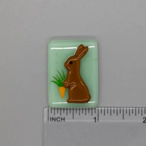 A chocolate bunny and carrot on a green background.