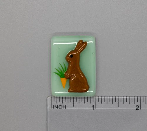 A chocolate bunny and carrot on a green background.