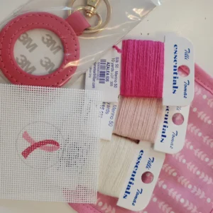 A pink ribbon is on the thread and some other items are laying out.