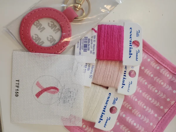 A pink ribbon is on the thread and some other items are laying out.