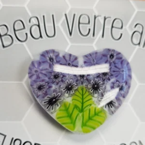 A heart shaped pin with purple and green flowers.