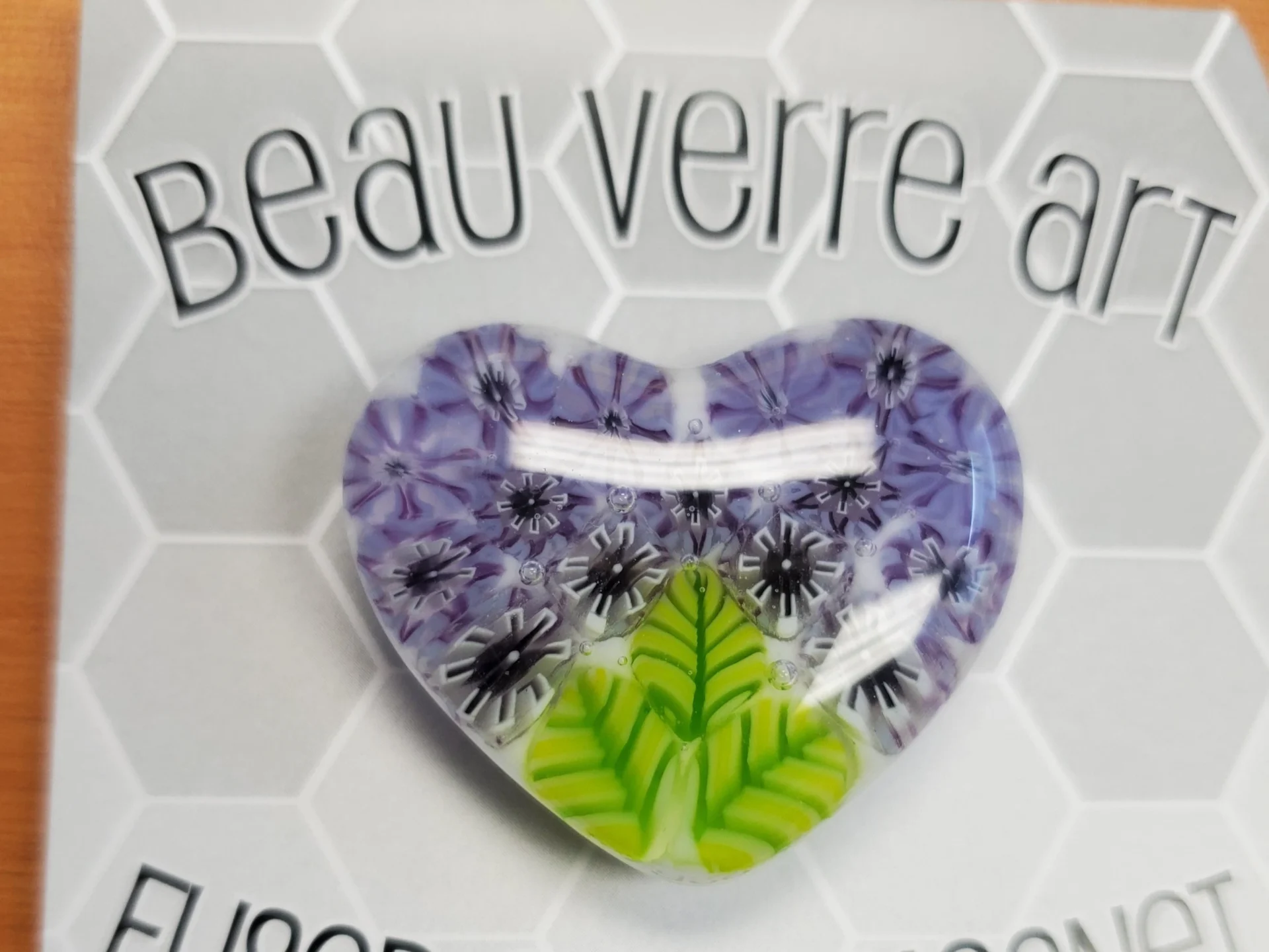 A heart shaped pin with purple and green flowers.