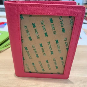 A pink wallet with some green stickers on it