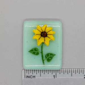 A small glass tile with a yellow flower on it.