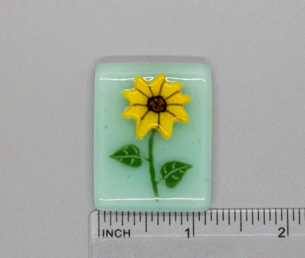 A small glass tile with a yellow flower on it.