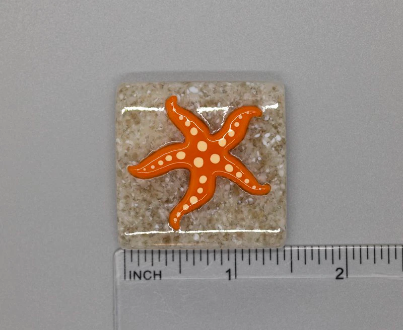 A square shaped tile with an orange starfish on it.