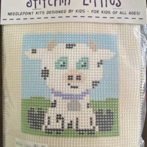 A cross stitch kit of a cow sitting on grass.