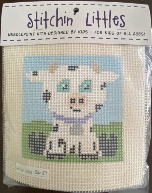 A cross stitch kit of a cow sitting on grass.